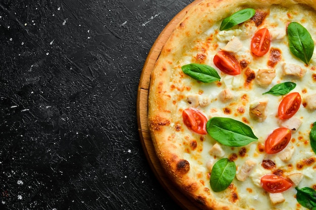 Pizza con tomate de pollo y espinaca pizza clásica sobre un fondo de piedra negra vista de arriba