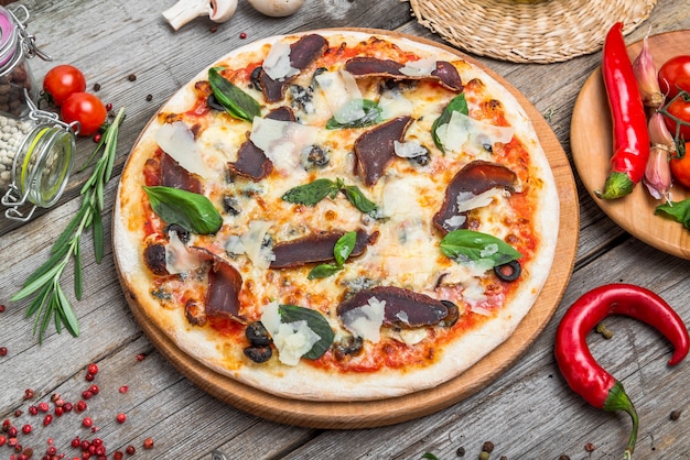 Pizza con tomate, queso mozzarella, aceitunas negras y albahaca