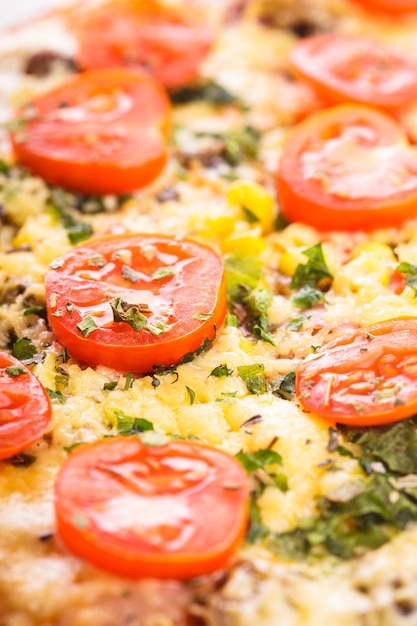 Pizza con tomates cherry y albahaca seca en el primer plano de la placa blanca de cerámica