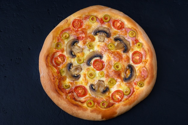 Pizza con tomates, mozzarella, salami, champiñones sobre fondo negro