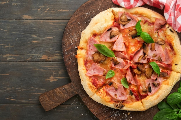 Pizza traditionelle Speckpizza mit Schinken, Pilzen, eingelegter Gurke und Käse und Kochzutaten, Tomaten, Basilikum auf Holztischhintergründen, italienisches traditionelles Essen, Ansicht von oben, Attrappe