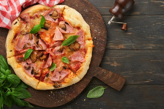 Pizza traditionelle Speckpizza mit Schinken, Pilzen, eingelegter Gurke und Käse und Kochzutaten, Tomaten, Basilikum auf Holztischhintergründen, italienisches traditionelles Essen, Ansicht von oben, Attrappe