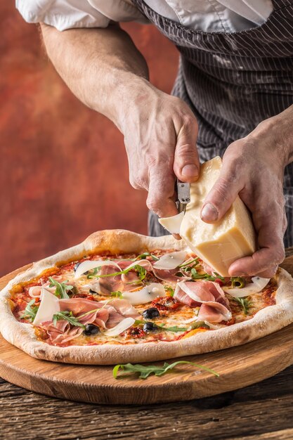 Pizza und Koch. Chefkoch im Restaurant bereitet eine Pizza zu und dekoriert sie mit Parmesankäse.