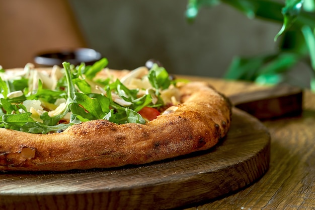 Pizza vegetariana al horno de leña con rúcula, verduras y parmesano sobre tablero de madera. Enfoque selectivo