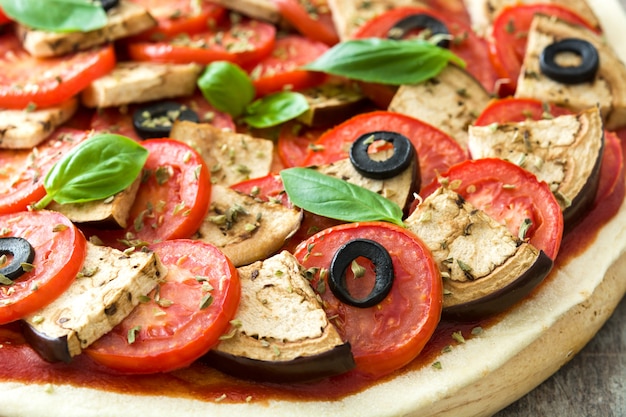 Pizza vegetariana con berenjenas, tomate, aceitunas negras, orégano y albahaca en mesa de madera de cerca