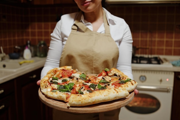 Pizza vegetariana casera al horno en una tabla de madera en manos de una encantadora ama de casa con delantal de chef