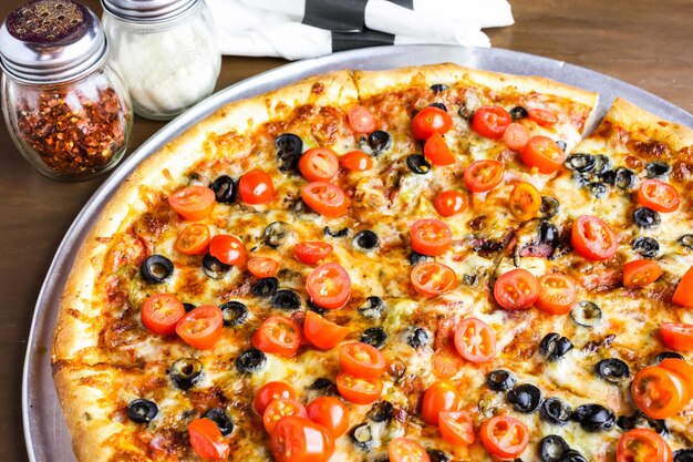 Pizza vegetariana com azeitonas e tomate cereja em cima da mesa.