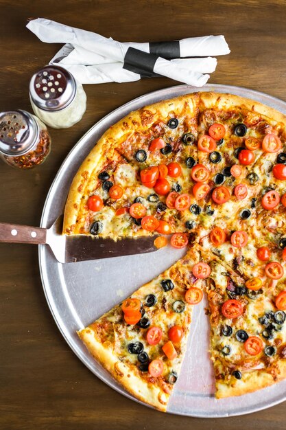 Pizza vegetariana com azeitonas e tomate cereja em cima da mesa.