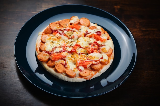 Pizza-, Wurst- und Krabbenstäbchen in einer Keramikplatte auf einem Holztisch.