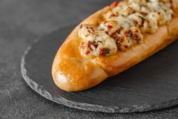 Pizzabaguette auf Schiefersteinplatte, runder dunkler Hintergrund, Seitenansicht, selektiver Fokus