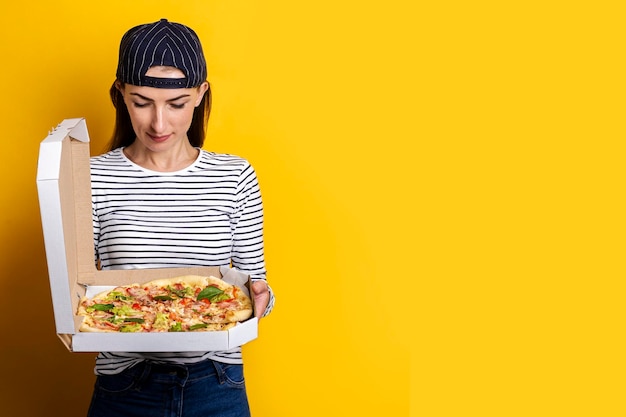 Pizzabote der jungen Frau, der Pizza auf gelbem Hintergrund hält