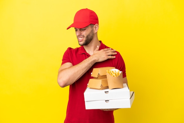 Pizzabote, der Pizzakartons und Burger über isoliertem Hintergrund abholt und unter Schmerzen in der Schulter leidet, weil er sich bemüht hat?