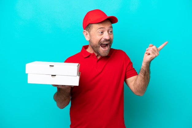 Pizzabote mit Arbeitsuniform, der Pizzakartons isoliert auf blauem Hintergrund aufhebt, um die Lösung zu realisieren, während er einen Finger hochhebt