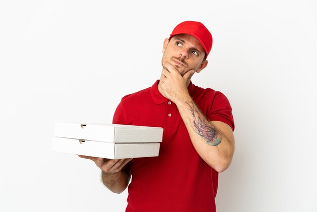 Pizzabote mit Arbeitsuniform, der Pizzakartons über isolierter weißer Wand abholt, die Zweifel hat