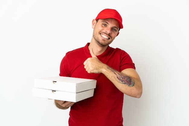 Pizzabote mit Arbeitsuniform, der Pizzakartons über isolierter weißer Wand aufhebt und eine Geste mit dem Daumen nach oben gibt