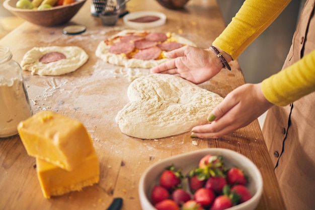 Pizzaherz mit Teig und Händen auf einem Holztisch. Person, die zu Hause mit Mehl und Käse, Obst und Essen kocht. Ernährungsmahlzeit und Erdbeere in der Küche, Backen mit Zutaten und Liebeszeichen