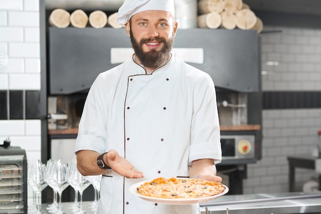 Pizzaiolo sonriente sosteniendo deliciosa pizza recién horneada deliciosa