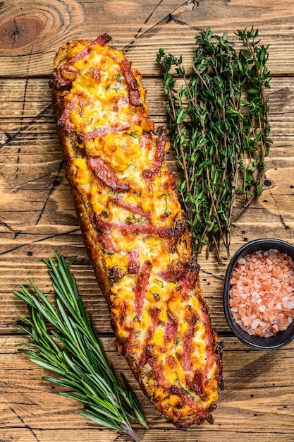 Pizzasandwich auf Baguettebrot mit Schinken, Speck, Gemüse und Käse auf Holztisch