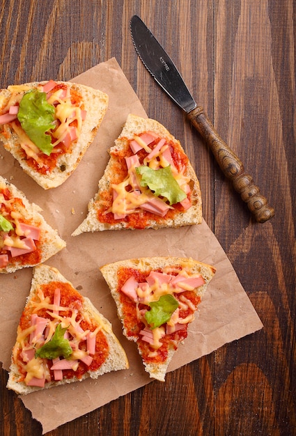 Pizzascheiben auf Pergament auf hölzernem Hintergrund