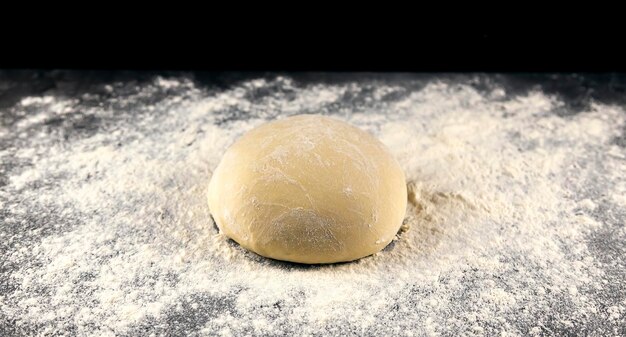 Pizzateig auf einem dunklen Tisch, bestreut mit Mehl. Backkonzept italienische Küche