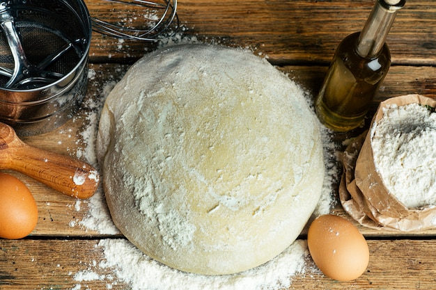 Pizzateig, der in der Hauptküche kocht. Hausgemachter Teig für Brot, Pizza, Gebäck und Brötchen. Teigbestandteile auf einem hölzernen rustikalen Hintergrund