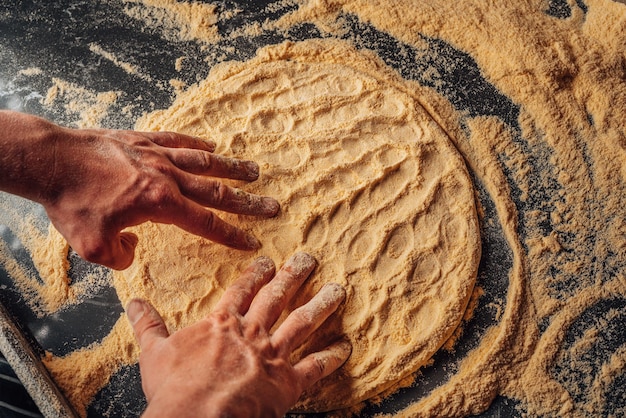 Pizzateig machen. Hände kneten einen Teig für eine Pizza, die mit Mehl auf dem Tisch kocht