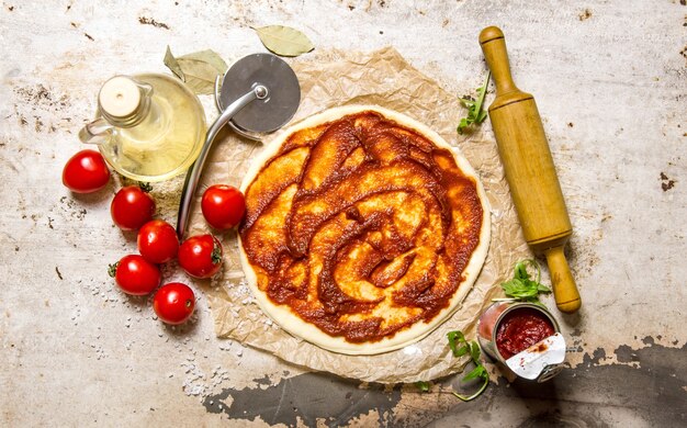 Pizzateig mit Tomatenmark und Nudelholz.