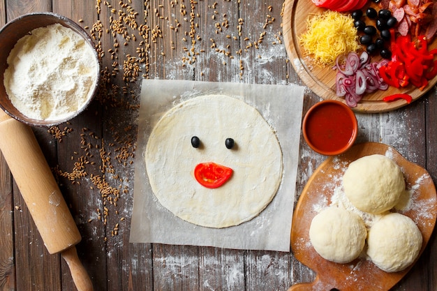 Pizzateig mit Zutaten auf Holztisch