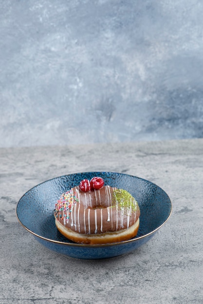 Foto placa azul com donut de chocolate com baga e granulado na superfície de mármore.