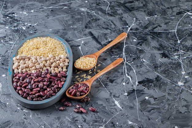 Placa azul llena de garbanzos crudos, arroz y frijoles sobre fondo de mármol.