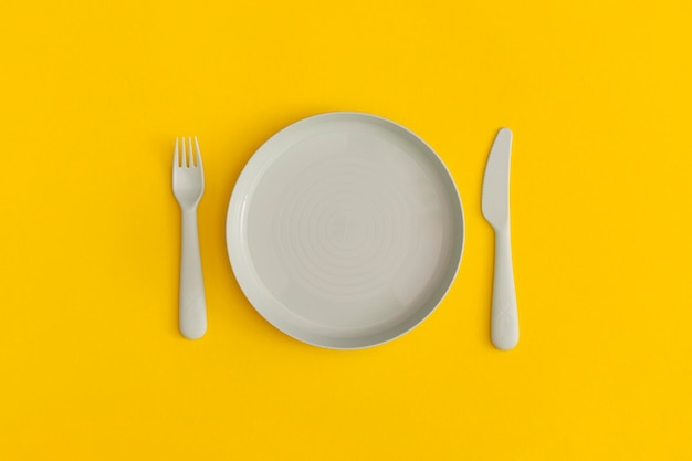 Placa azul con tenedor y cuchara sobre un fondo amarillo. Vista superior. Endecha plana.