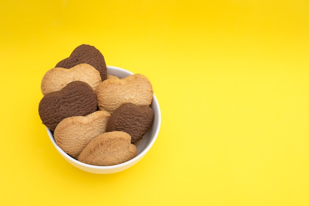 Placa blanca con galletas multicolores en forma de corazón sobre una mesa amarilla