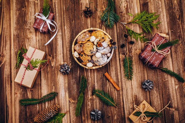 Placa com biscoitos de Natal fica na mesa com presentes, ramos e cones de abeto