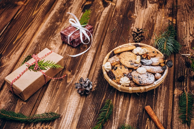 Placa com biscoitos de natal fica na mesa com presentes, ramos e cones de abeto