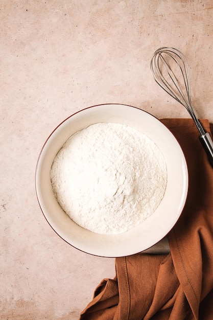 Placa de concepto de fondo de alimentos con batidor de harina de trigo para batir una toalla de cocina en una vista de mesa beige rústica