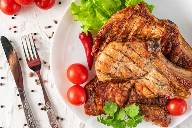 Placa de cerâmica branca com carne de porco grelhada, folhas de alface, tomate e pimenta vermelha e molho nas tigelas