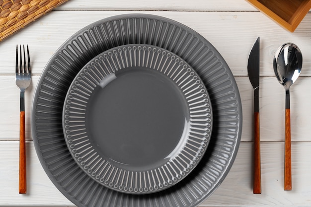 Placa de cerâmica cinza brilhante com talheres na mesa da cozinha de madeira