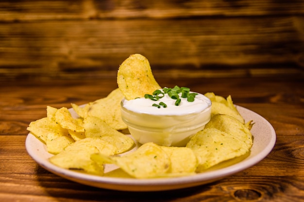 Placa de cerâmica com batatas fritas e tigela de vidro com creme azedo na mesa de madeira