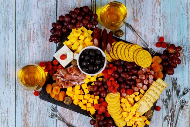 Placa de charcutaria com queijo, azeitonas, frutas, presunto e vinho na mesa de madeira