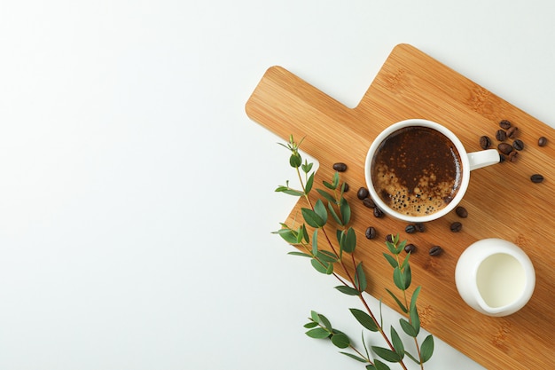 Placa de corte com uma xícara de leite fresco, grãos de café e ramo de planta em fundo branco