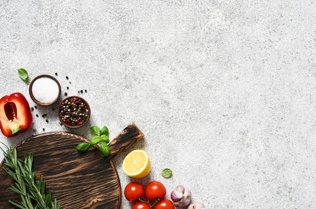 Placa de corte marrom com especiarias e vegetais em uma luz, uma mesa de cozinha de concreto.