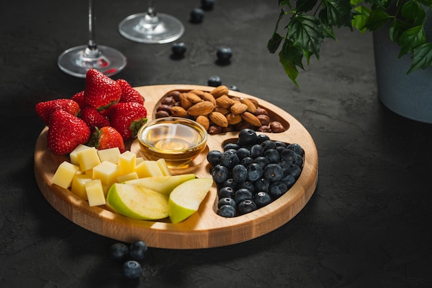 Placa de madeira com frutas e nozes em um fundo escuro Frutas em um fundo preto