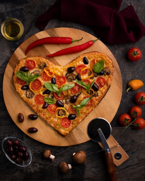 Placa de madeira com pizza caseira em forma de coração com ingredientes em fundo preto celebração do dia dos namorados