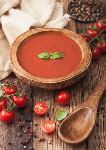 Placa de madeira de sopa cremosa de tomate com colher de pau, pimenta e pano de cozinha na placa de madeira. com tomates crus.