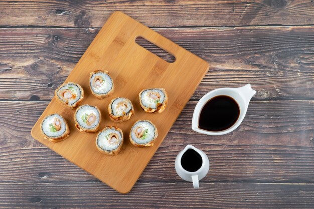 Placa de madeira de tempura sushi rolos e molho de soja na mesa de madeira.