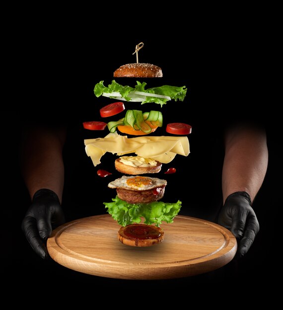 Foto placa de madeira e camadas de um grande cheeseburger flutuando no ar