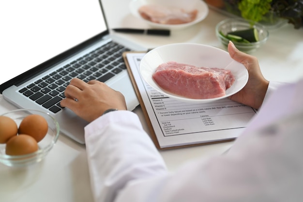 Placa de manutenção de nutricionista com carne crua dando consulta on-line ao paciente via laptop