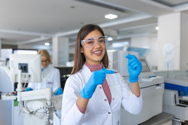 Placa de Petri na mão do jovem cientista perto do microscópio no laboratório Exame de placa de cultura bacteriana por uma pesquisadora no laboratório de microbiologia