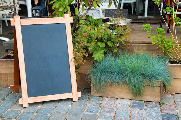 Placa de publicidade de menu vazio e caixa de madeira de grama perto de um restaurante