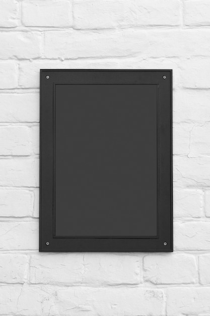 Foto placa de sinal preta ou moldura com espaço em branco para seu projeto em um fundo de parede de tijolo.